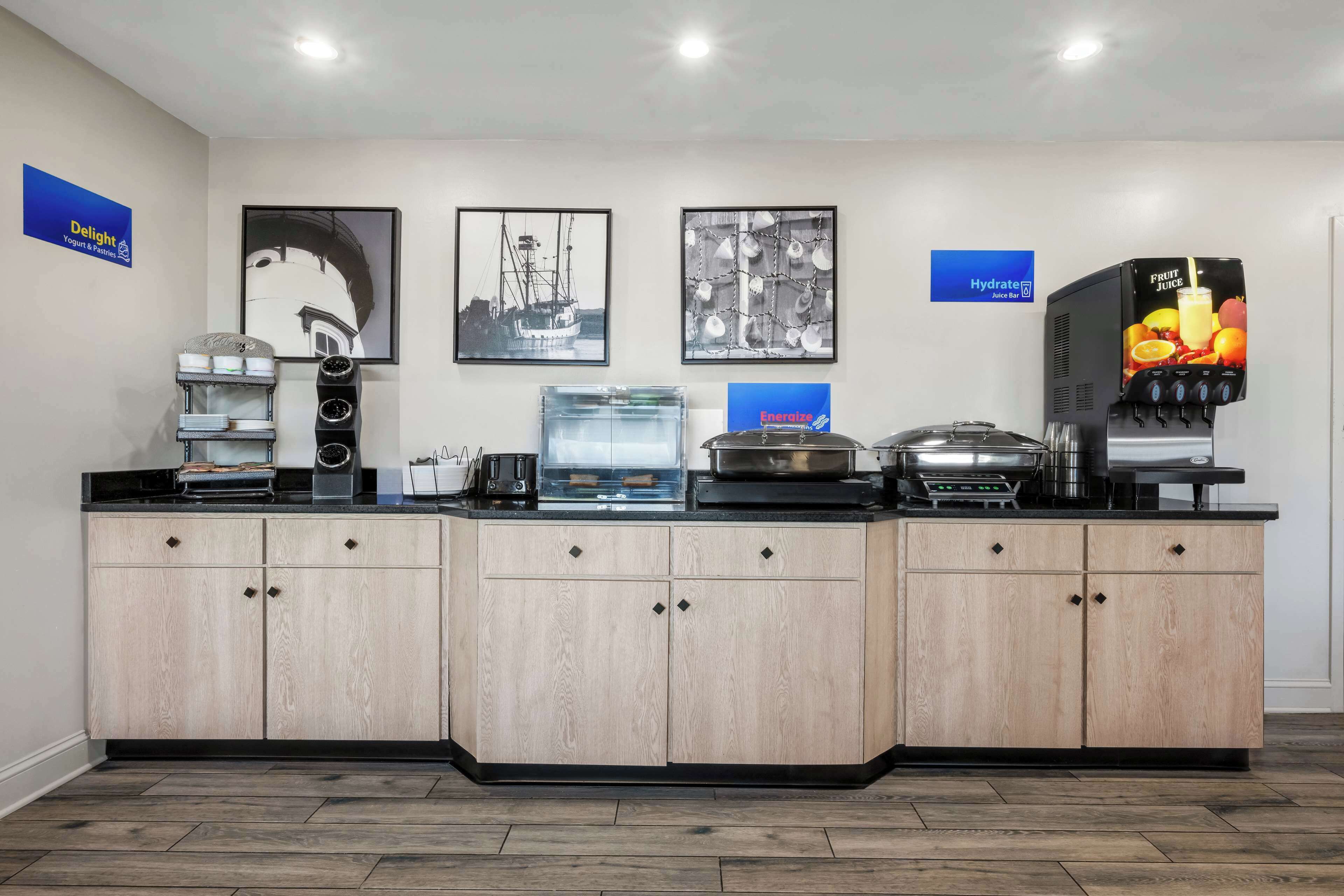 A modern kitchen with a coffee station, juice dispenser, and a refrigerator.