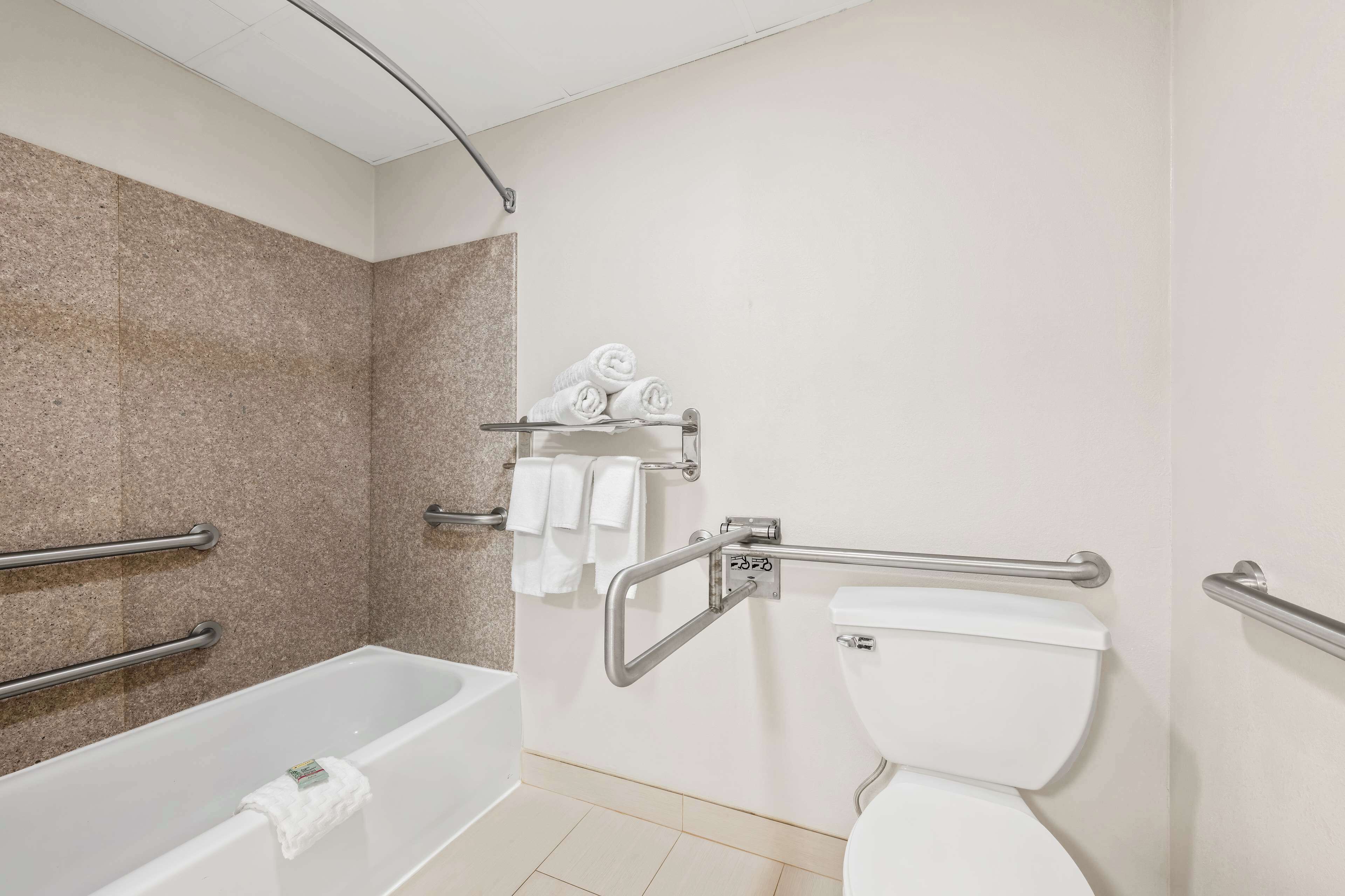 A bathroom with a bathtub, toilet, and handrails.