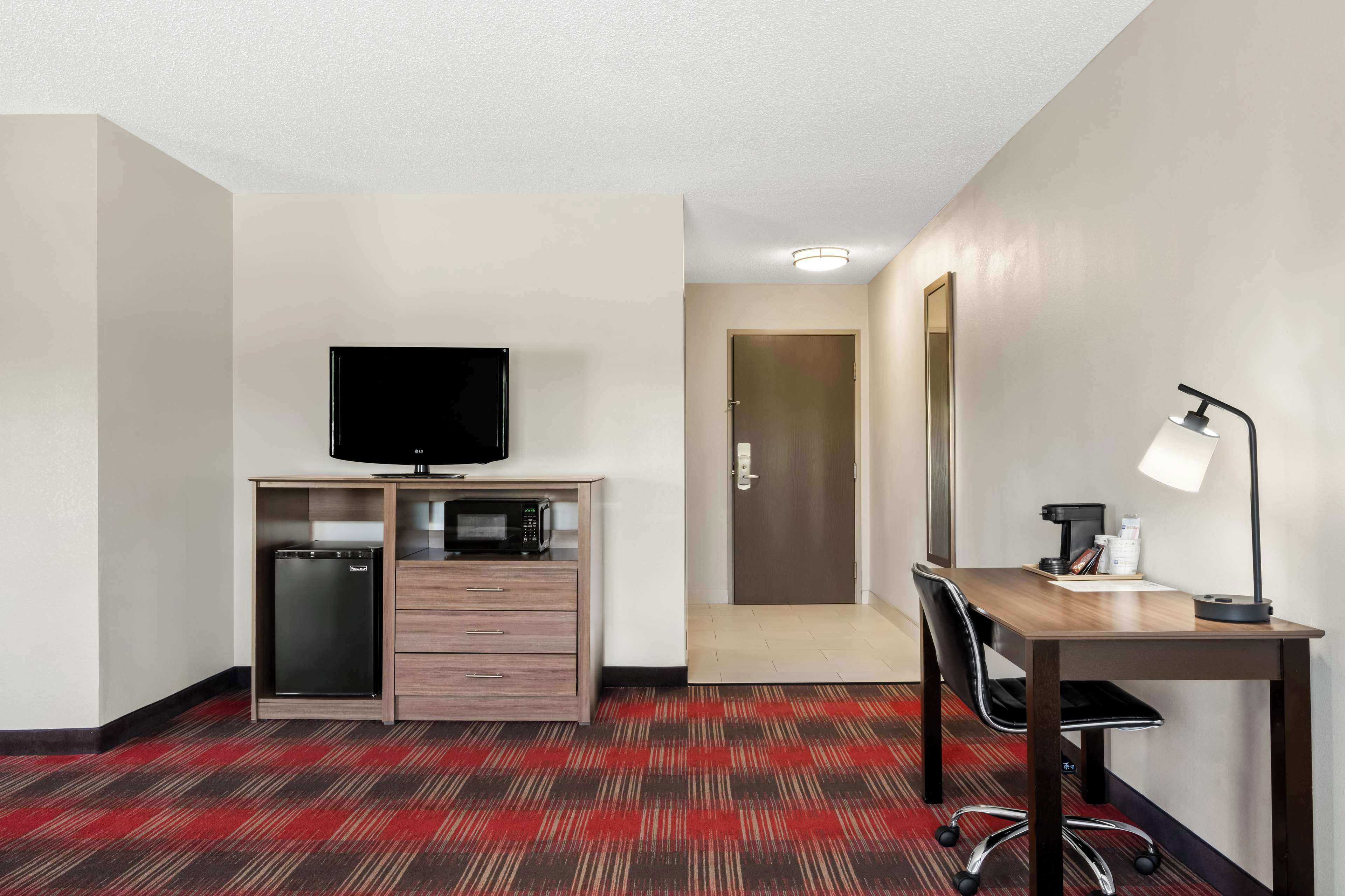 Een hotelkamer met een kitchenette, een flatscreen-tv, een bureau met een lamp en een deur naar een andere kamer.