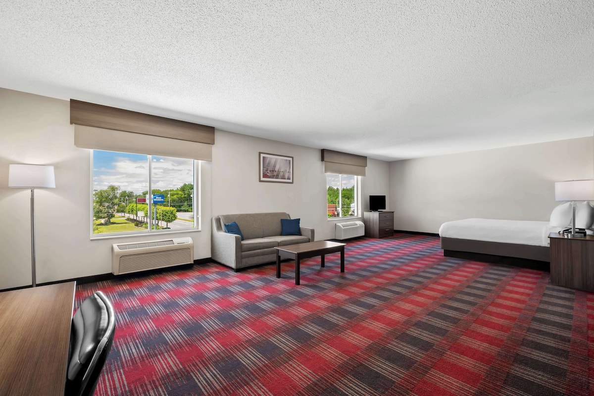 A hotel room with a large window, a sofa, a bed, a coffee table, and a carpeted floor.
