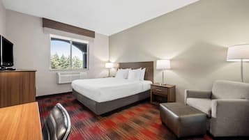 Une chambre d’hôtel équipée d’un lit, d’un bureau, d’une chaise, d’une télévision et d’une fenêtre donnant sur des arbres.