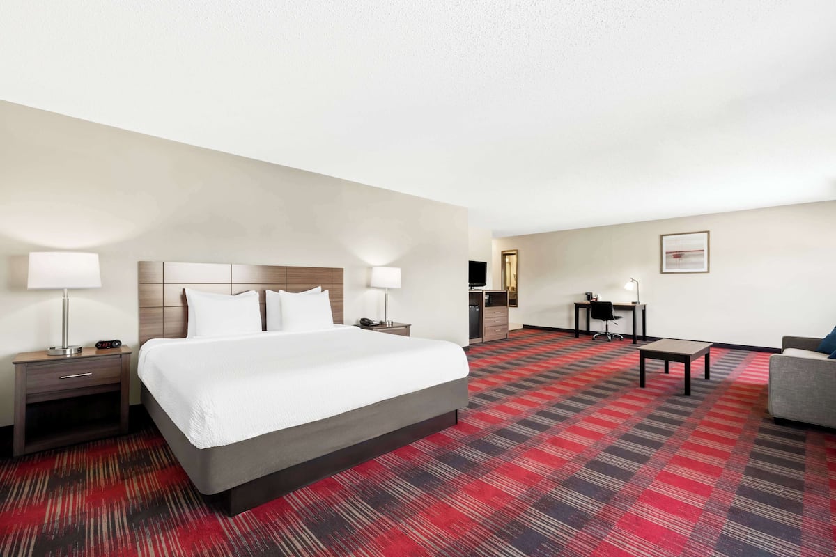 A hotel room with a large bed, a desk, a chair, and a sofa.