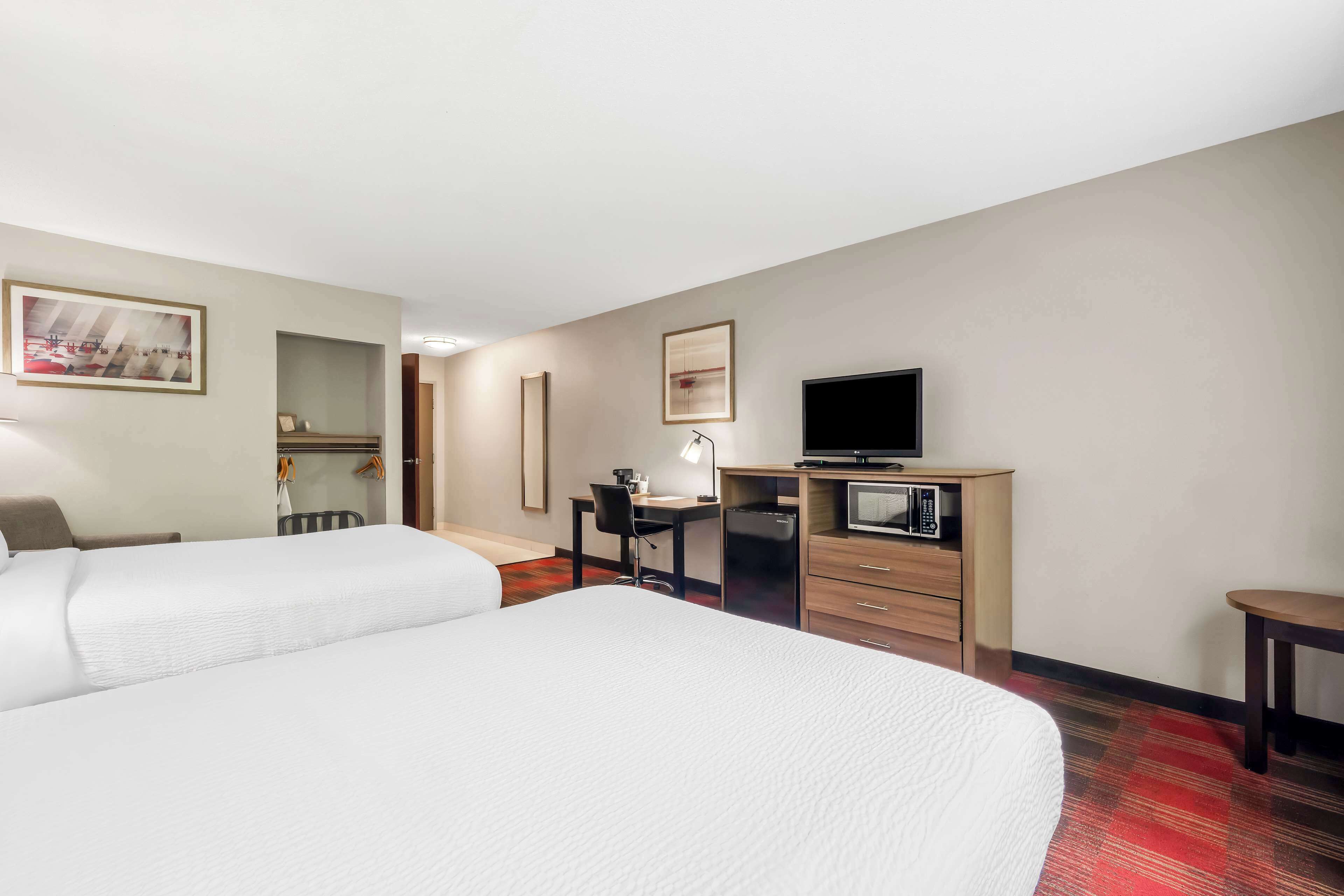 A hotel room with two beds, a desk with a computer, a television, and a microwave.