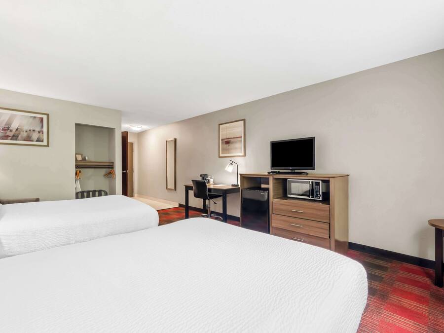 A hotel room with two beds, a desk with a computer, a television, and a microwave.