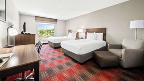 A hotel room with two beds, a desk, a chair, and a view of the outdoors.