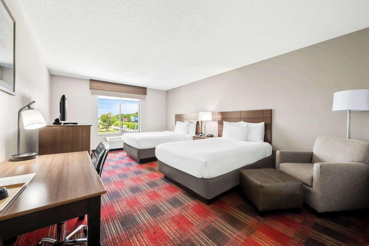 A hotel room with two beds, a desk, a chair, and a view of the outdoors.