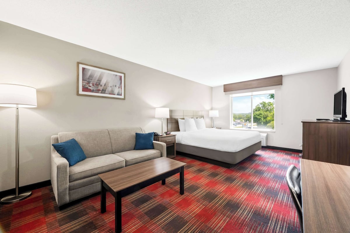 A hotel room with a bed, a sofa, a desk, and a lamp.