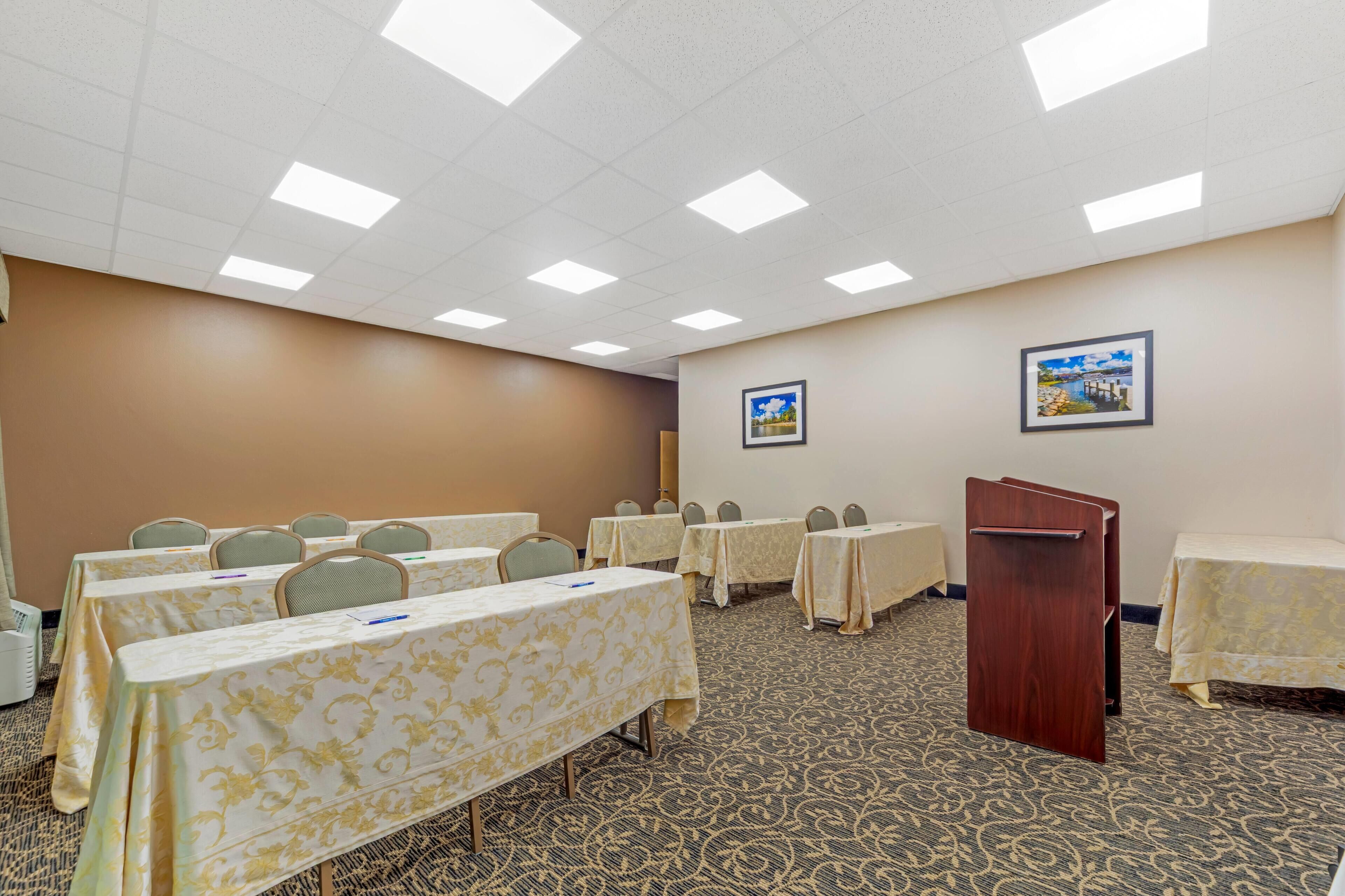 A conference room with tables, chairs, a podium, and framed pictures on the walls.