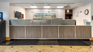 A reception area with a modern design, featuring a reception desk, a mounted television, a clock, and a large painting on the wall. - Wingate by Wyndham North East (North East)