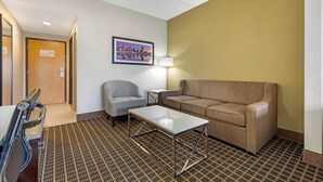A hotel room with a patterned carpet, a sofa, a chair, a small table, and a lamp. - Wingate by Wyndham North East (North East)