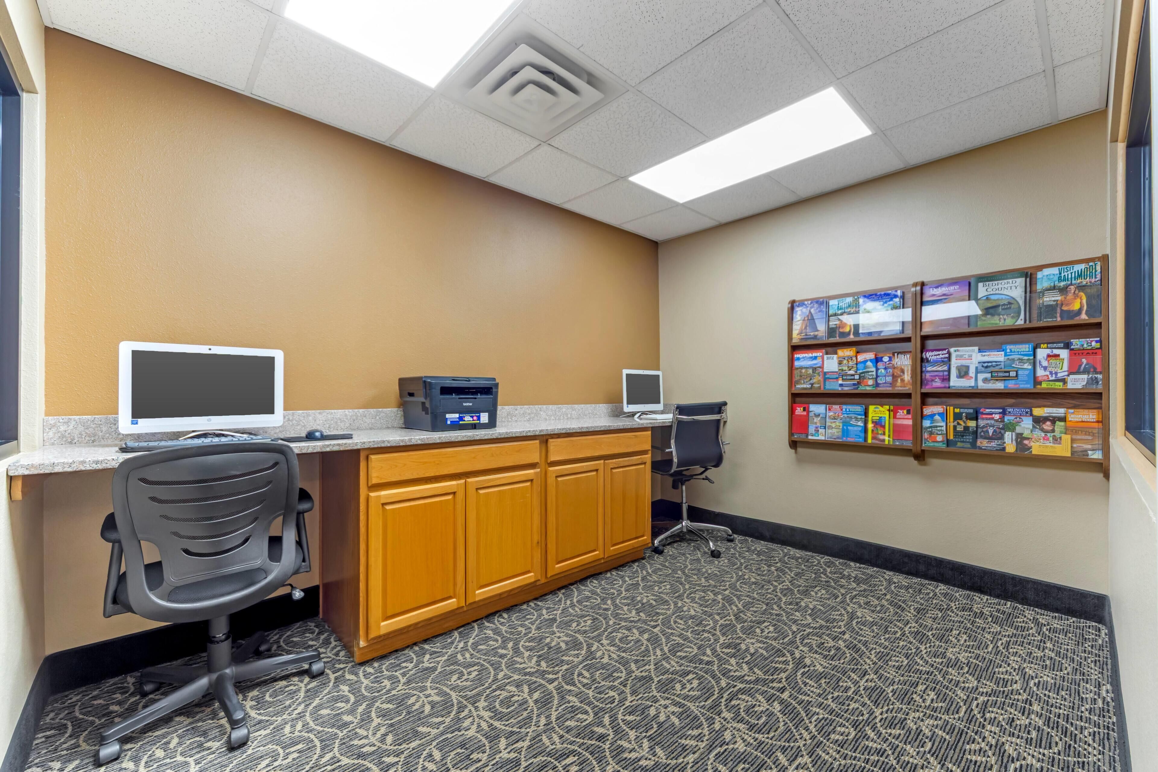 A reception area with a desk, two monitors, a printer, a chair, and a bookshelf with various books.