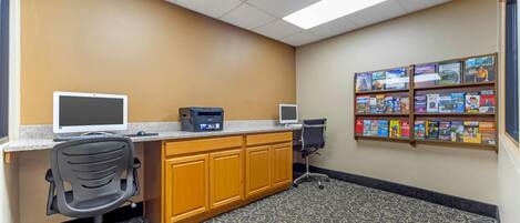 A reception area with a desk, two monitors, a printer, a chair, and a bookshelf with various books.