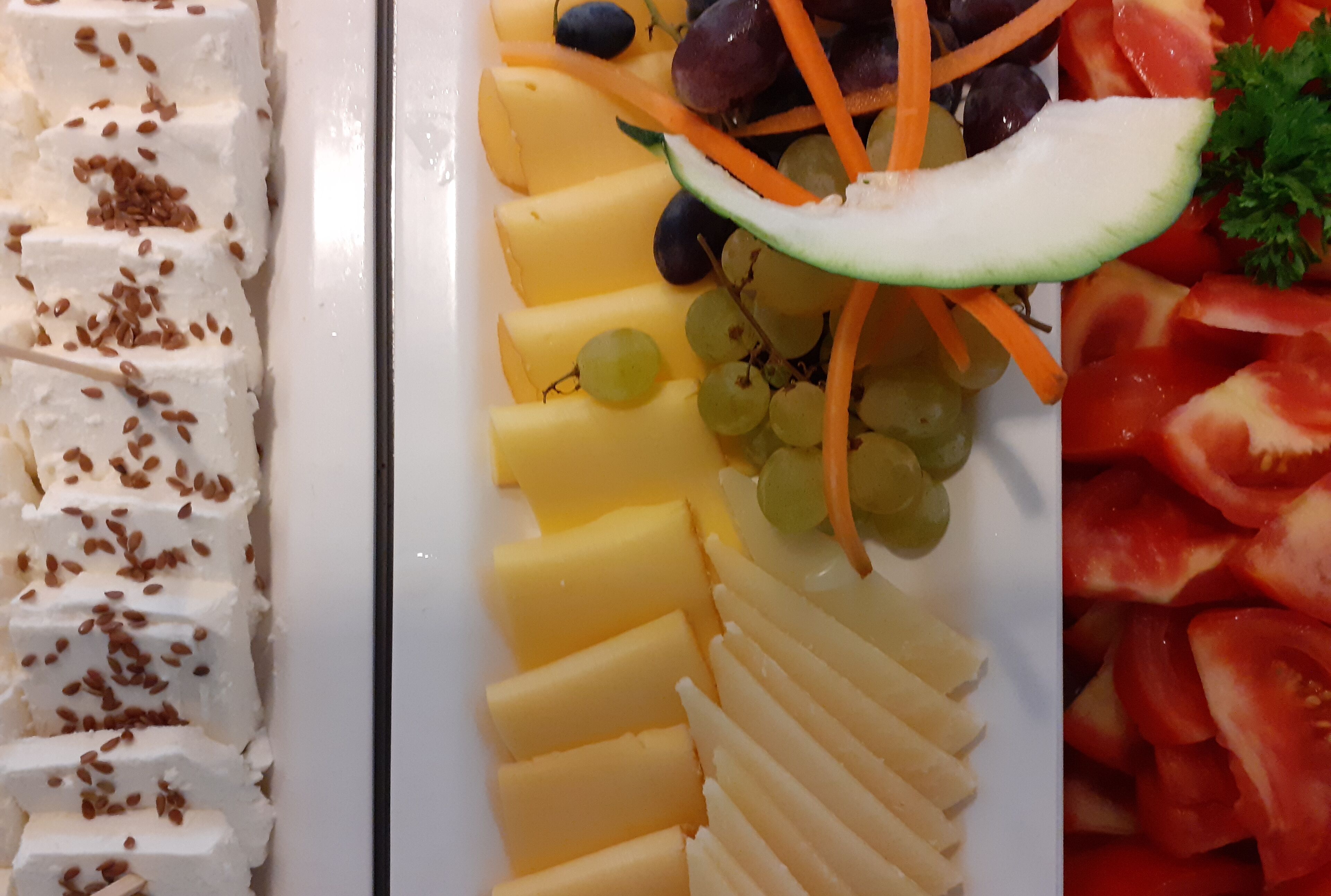 A platter of assorted cheeses, grapes, and sliced vegetables.