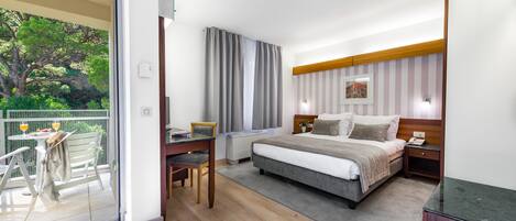 Una habitación de hotel moderna con una cama grande, un escritorio y un balcón con vistas a árboles.
