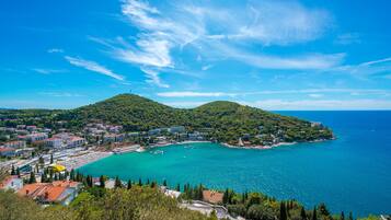 A coastal town with a clear blue sea, a small bay, and a hill with buildings.