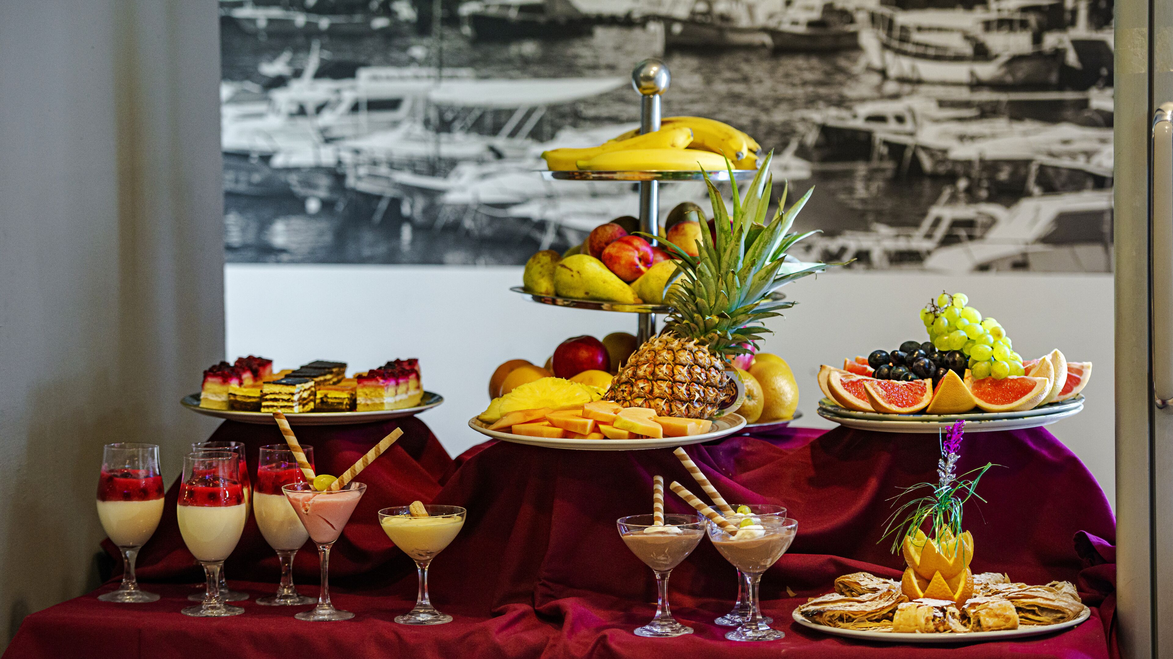 Een tafel met verschillende desserts en fruit, een bord oysters, en een zwart-wit foto op de achtergrond.