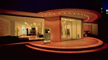 A modern hotel exterior with a curved facade, large glass entrance, and a well-lit interior visible through the windows.