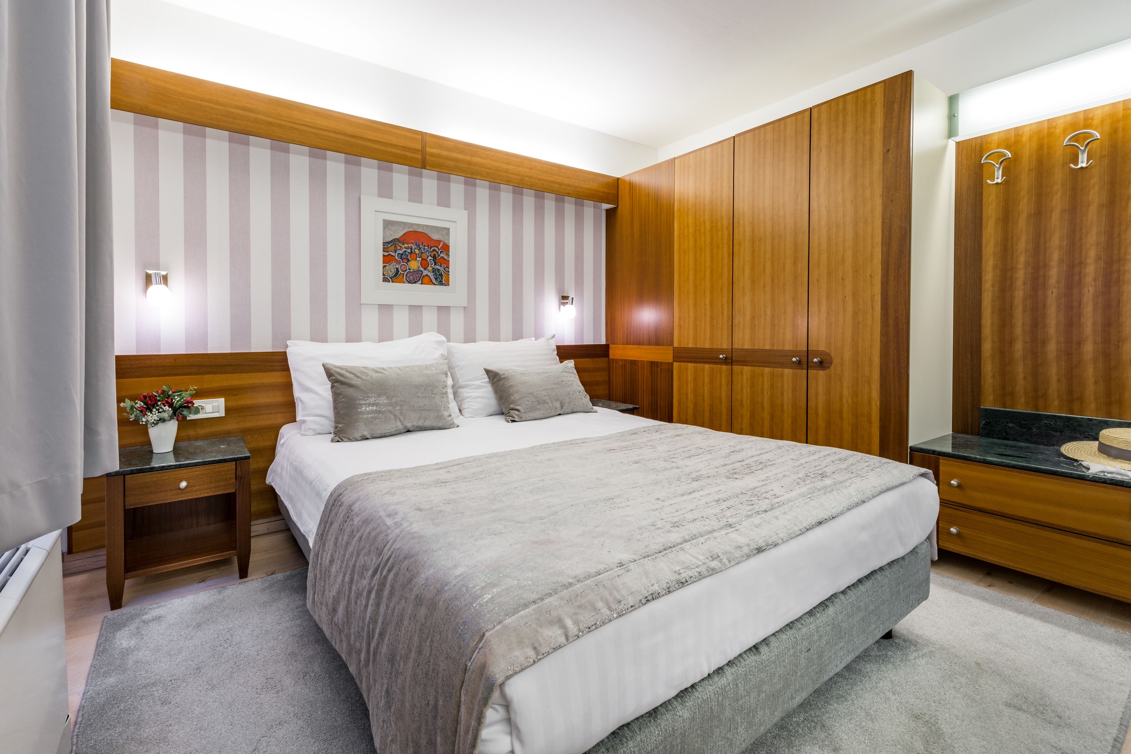 A bedroom with a large bed, wooden wardrobe, and a nightstand with a lamp.