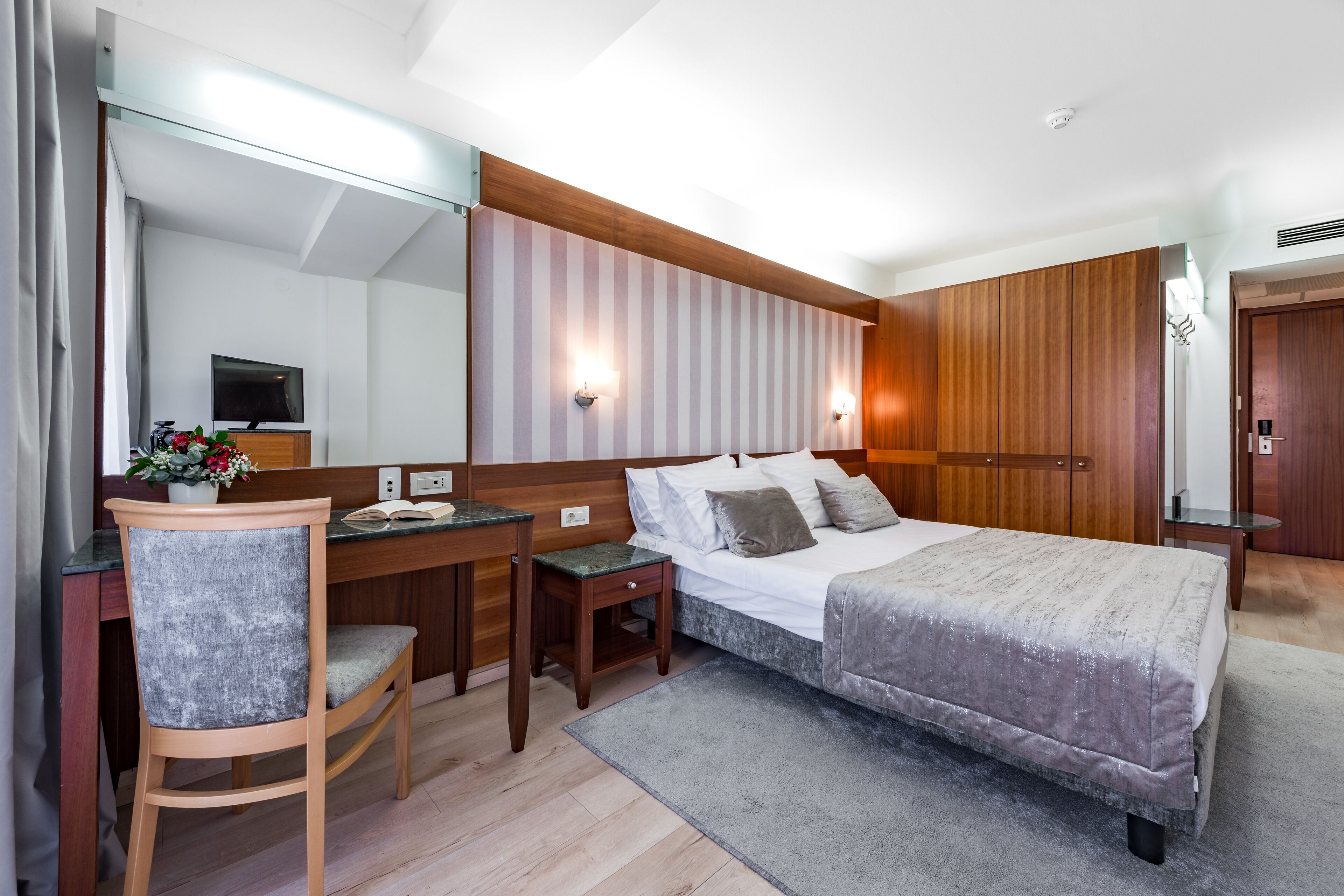 A modern bedroom with a bed, bedside tables, a desk, a chair, and a large mirror.