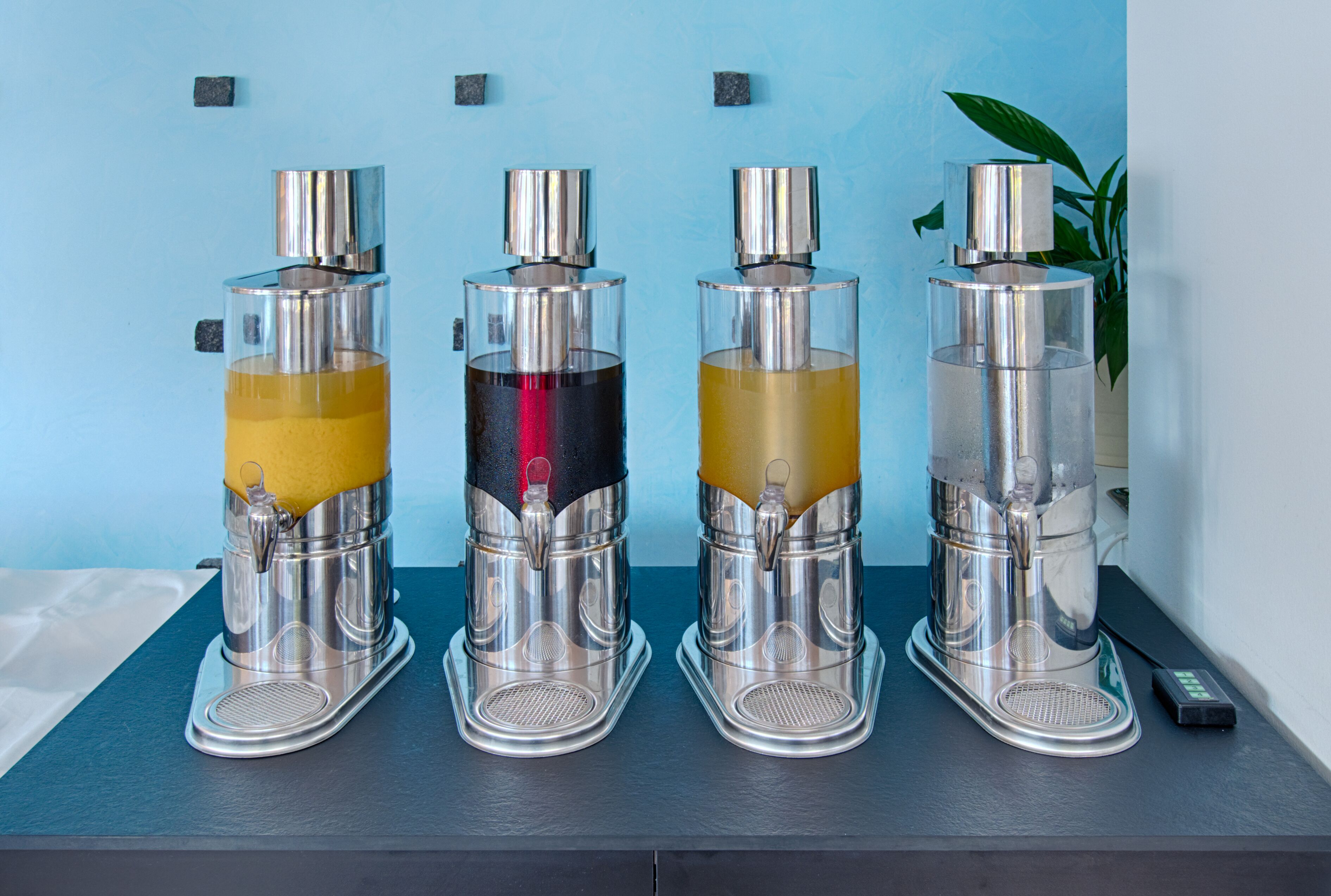 Cuatro máquinas de café con líquidos de colores distintos sobre una encimera frente a una pared azul.