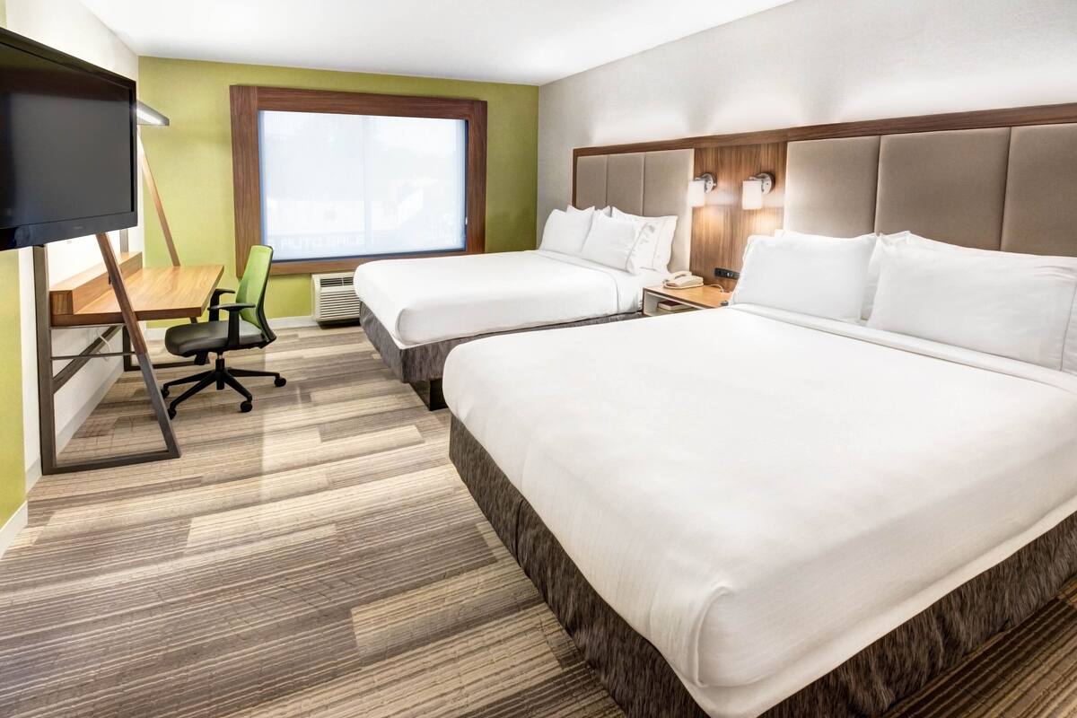 Une chambre d’hôtel avec deux lits, un bureau, une chaise, une télévision et une fenêtre.