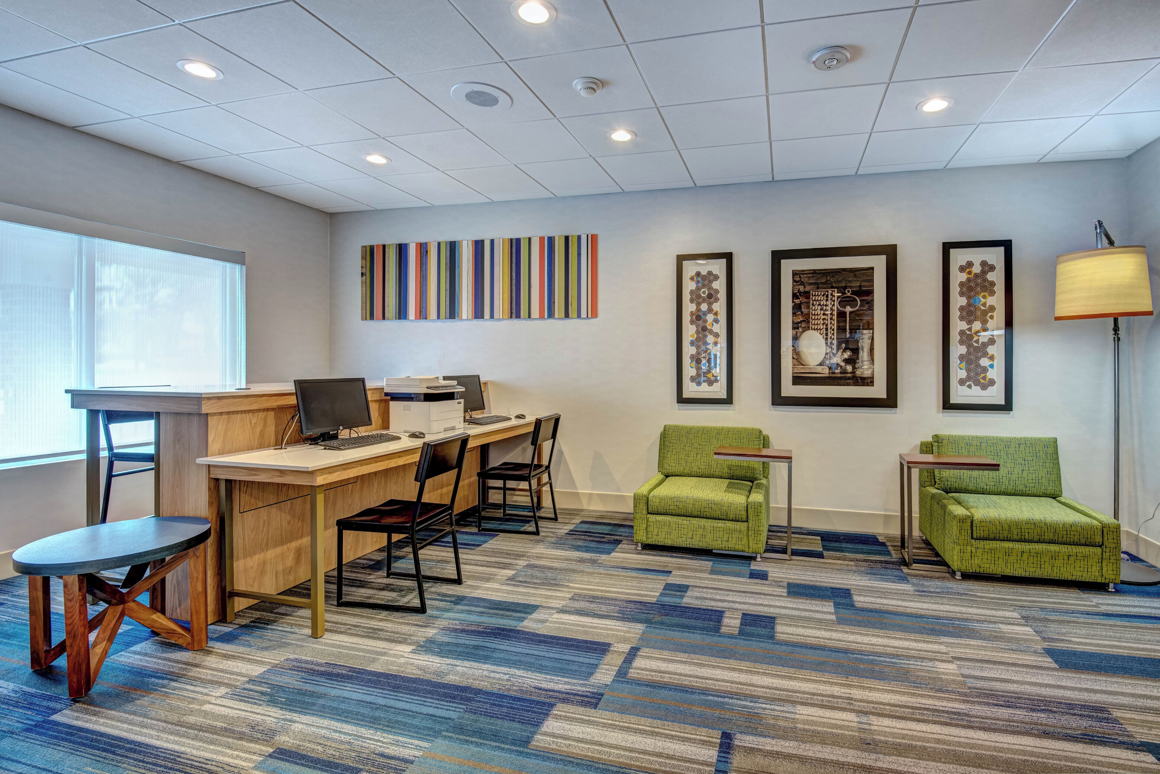 A modern office space with a desk, chairs, a computer, and framed artwork on the wall.