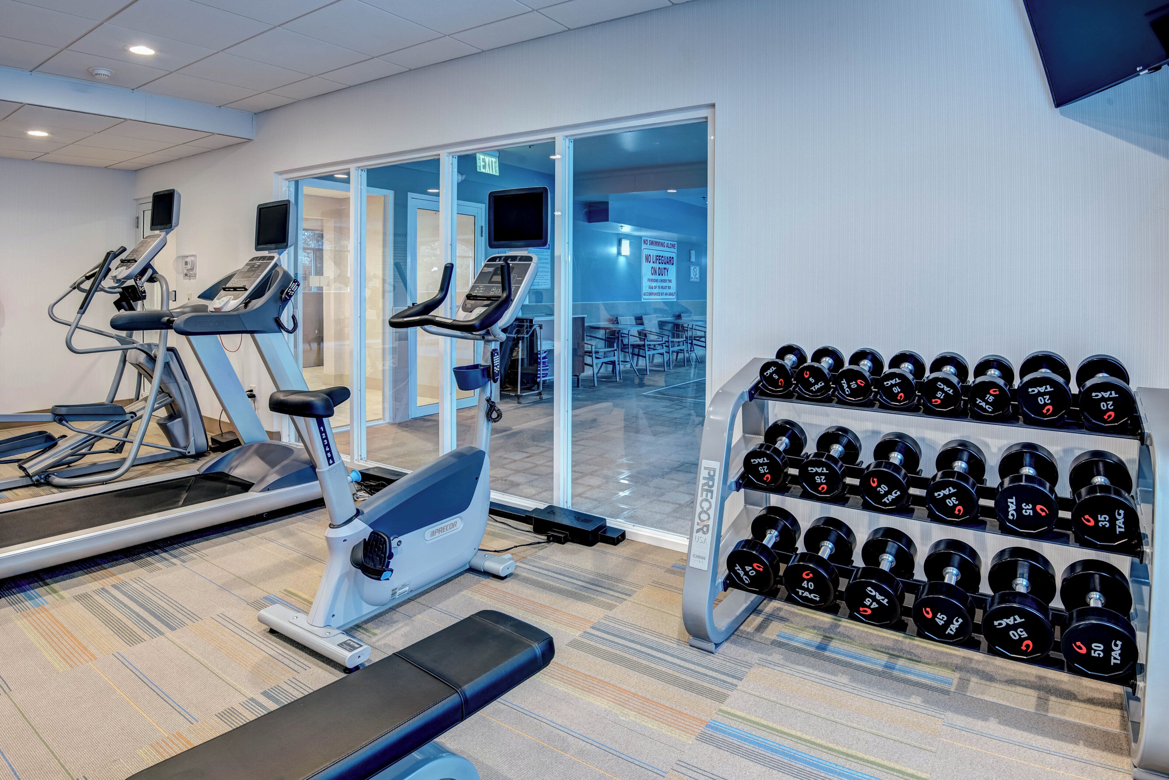 A gym with treadmills, an elliptical, and a rack of dumbbells.