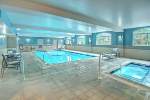 A swimming pool area with a tiled floor, lounge chairs, and a small seating area with tables.