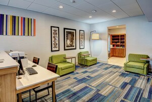 A modern office space with a reception desk, green armchairs, a patterned carpet, and framed artwork on the walls.