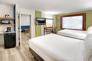 Quarto de hotel com cama, televisão, escrivaninha, micro-ondas e cafeteira.