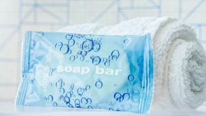 A soap bar and a rolled white towel on a white surface. - Holiday Inn Express Woodbridge by IHG (Avenel)