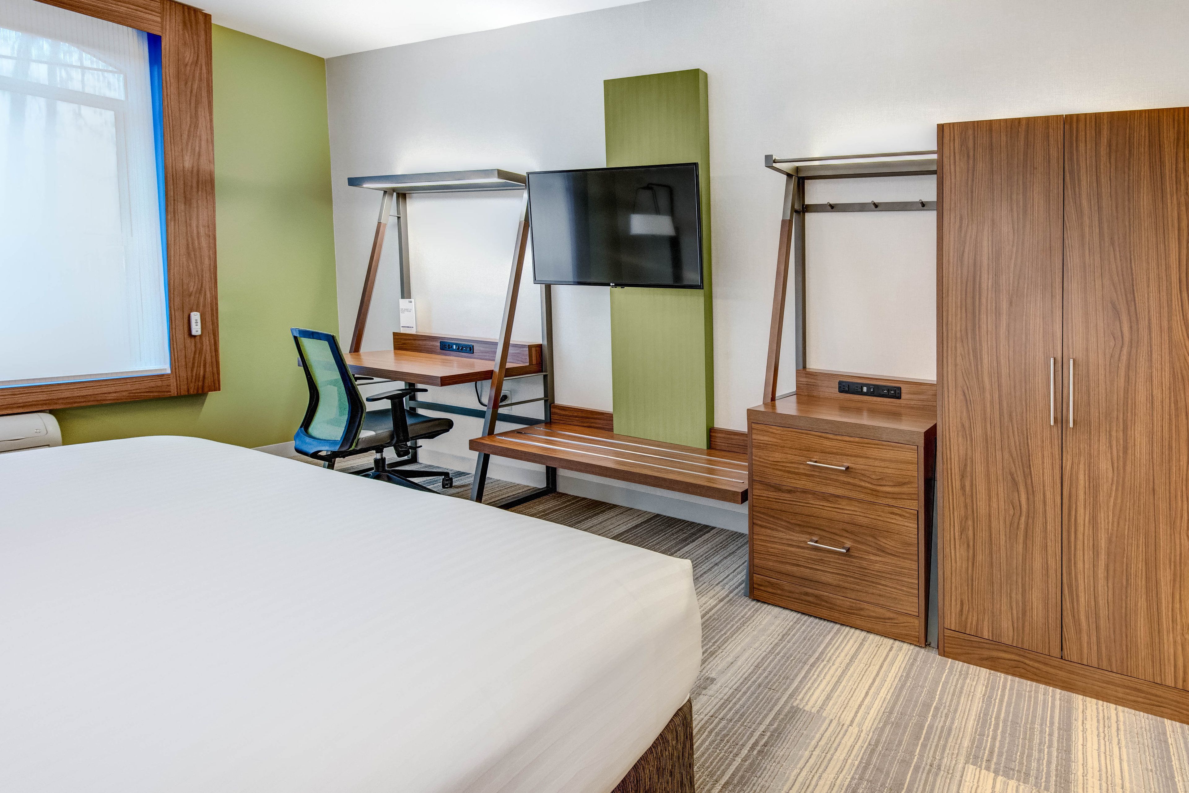 A hotel room with a bed, desk, chair, TV, wardrobe, and a window.