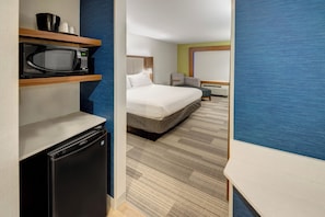 Habitación de hotel con cama, microondas, refrigerador y zona de estar con una silla y una mesita.