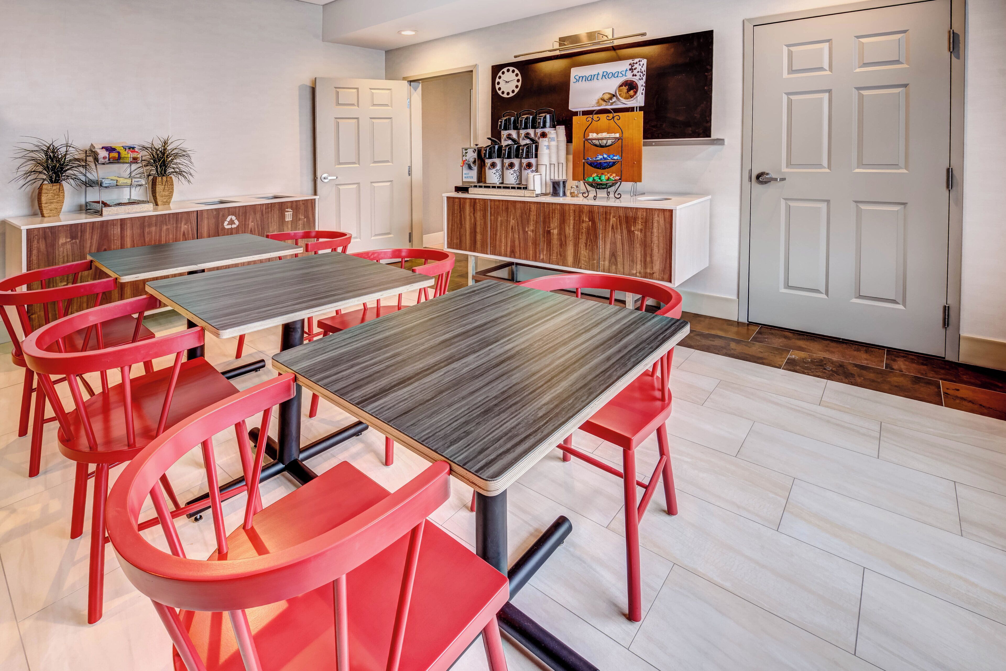 Un comedor con sillas y mesas rojas, una zona de cocina con un letrero que dice 'Smart Roast', y un reloj en la pared.