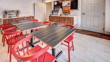 Un comedor con sillas y mesas rojas, una zona de cocina con un letrero que dice 'Smart Roast', y un reloj en la pared.