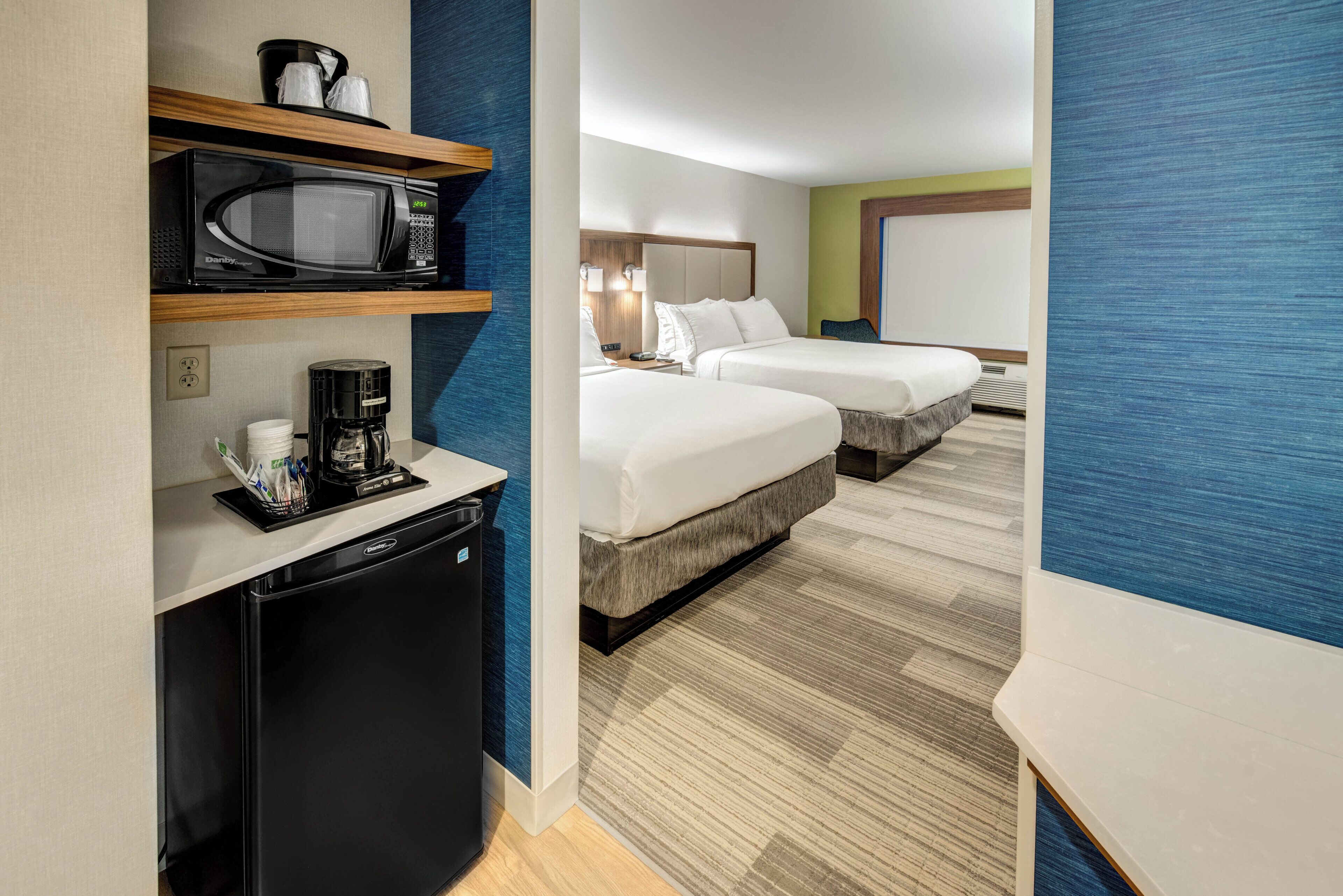Habitación de hotel con kitchenette, dos camas, un refrigerador pequeño y un microondas.