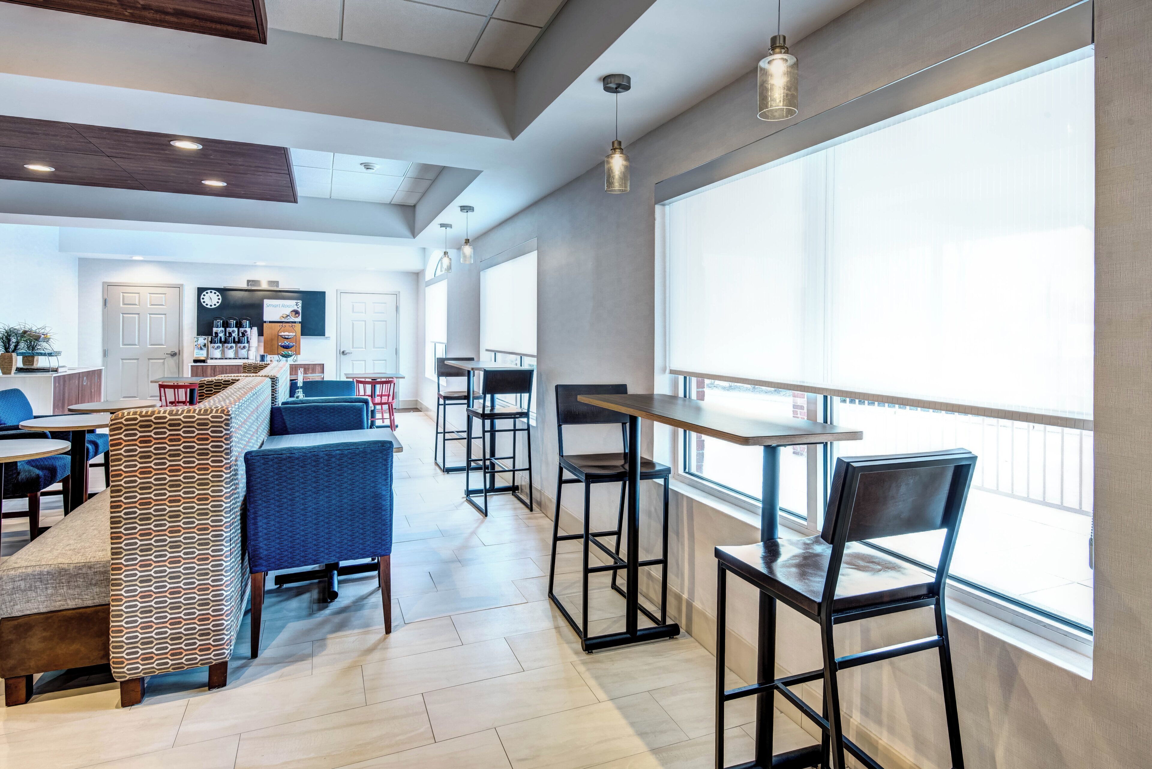 Un café moderne avec des tables et des chaises hautes, une machine à café et une horloge au mur.