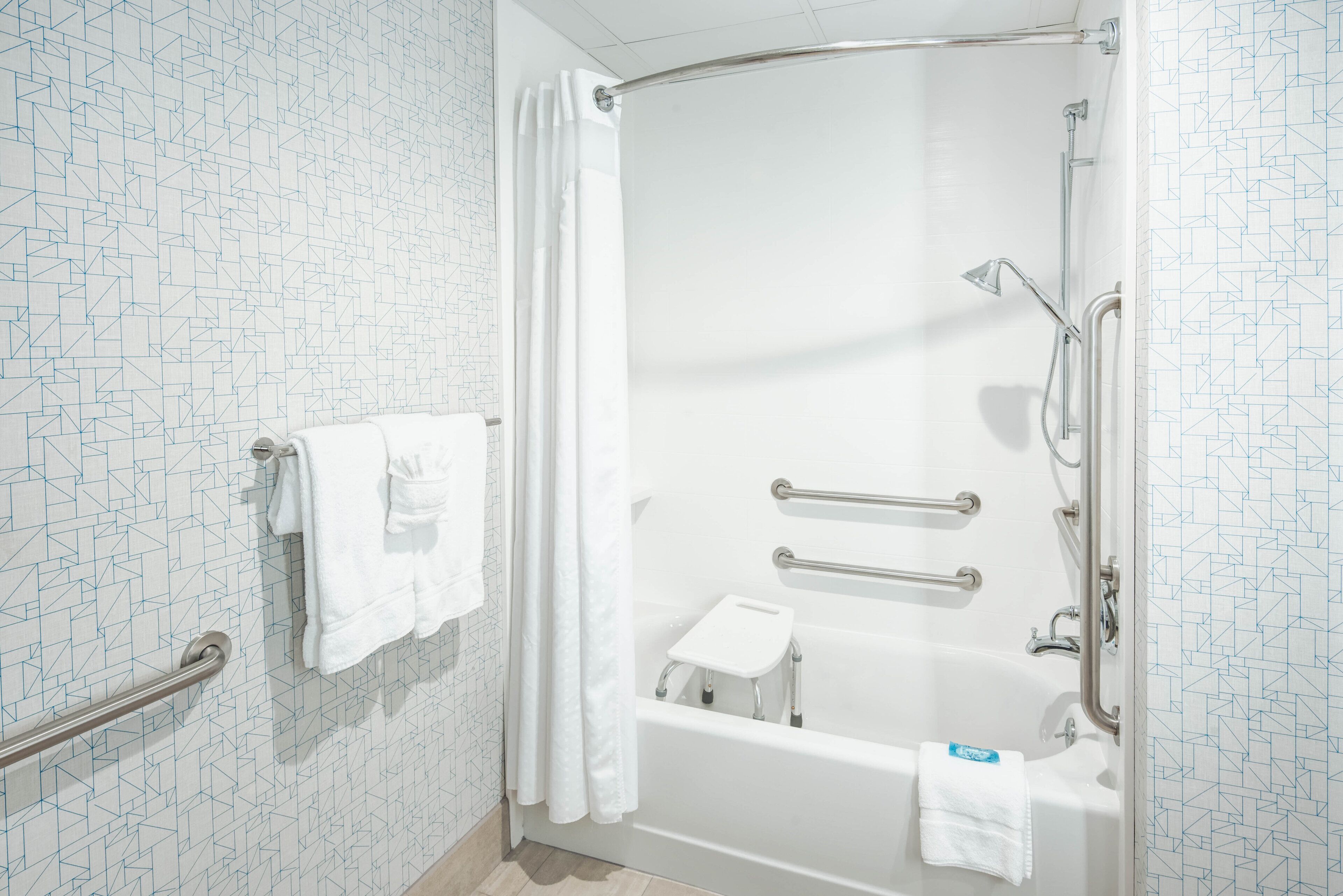 A modern bathroom with a walk-in shower, grab bars, a white towel, and a small step stool.
