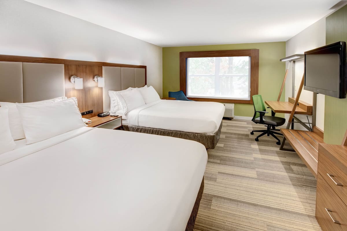 Une chambre d’hôtel avec deux lits, un bureau, une chaise, une télévision et une fenêtre.