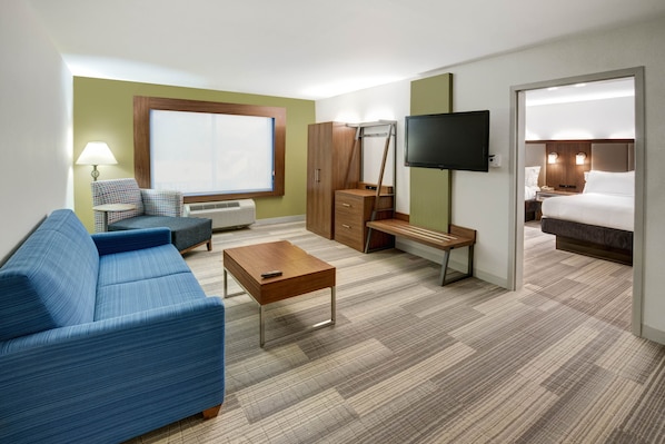 Habitación de hotel con sofá azul, mesa de centro de madera, escritorio, armario, televisor y cama.