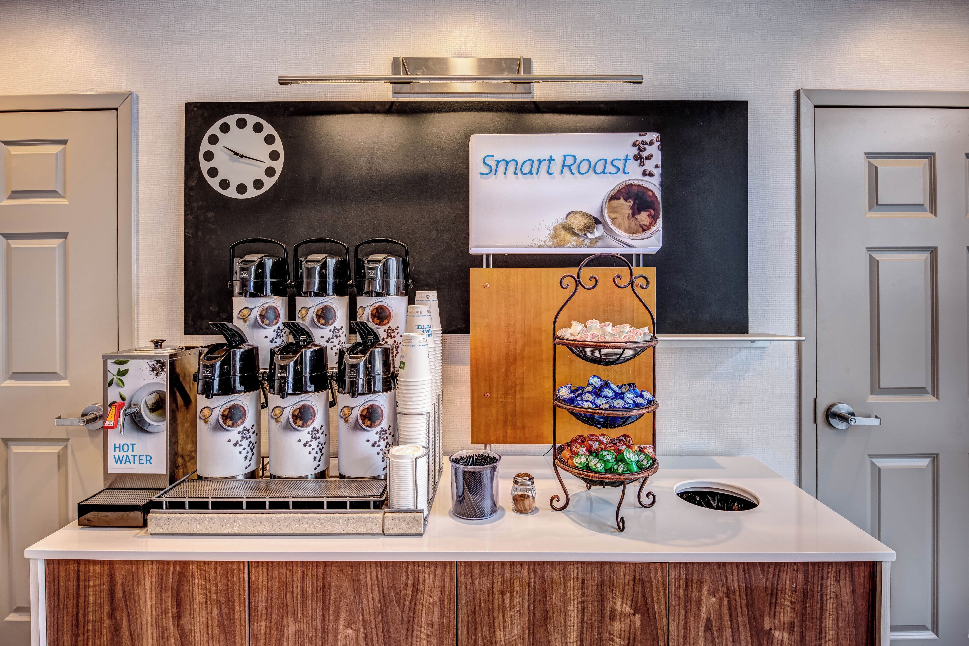 A coffee station with multiple coffee machines, a sign reading 'Smart Roast,' and a clock on the wall.