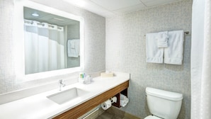 A modern bathroom with a large mirror, white sink, wooden vanity, and a toilet. - Holiday Inn Express Woodbridge by IHG (Avenel)