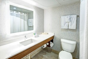 Un baño moderno con un espejo grande, lavabo blanco, tocador de madera y un inodoro.