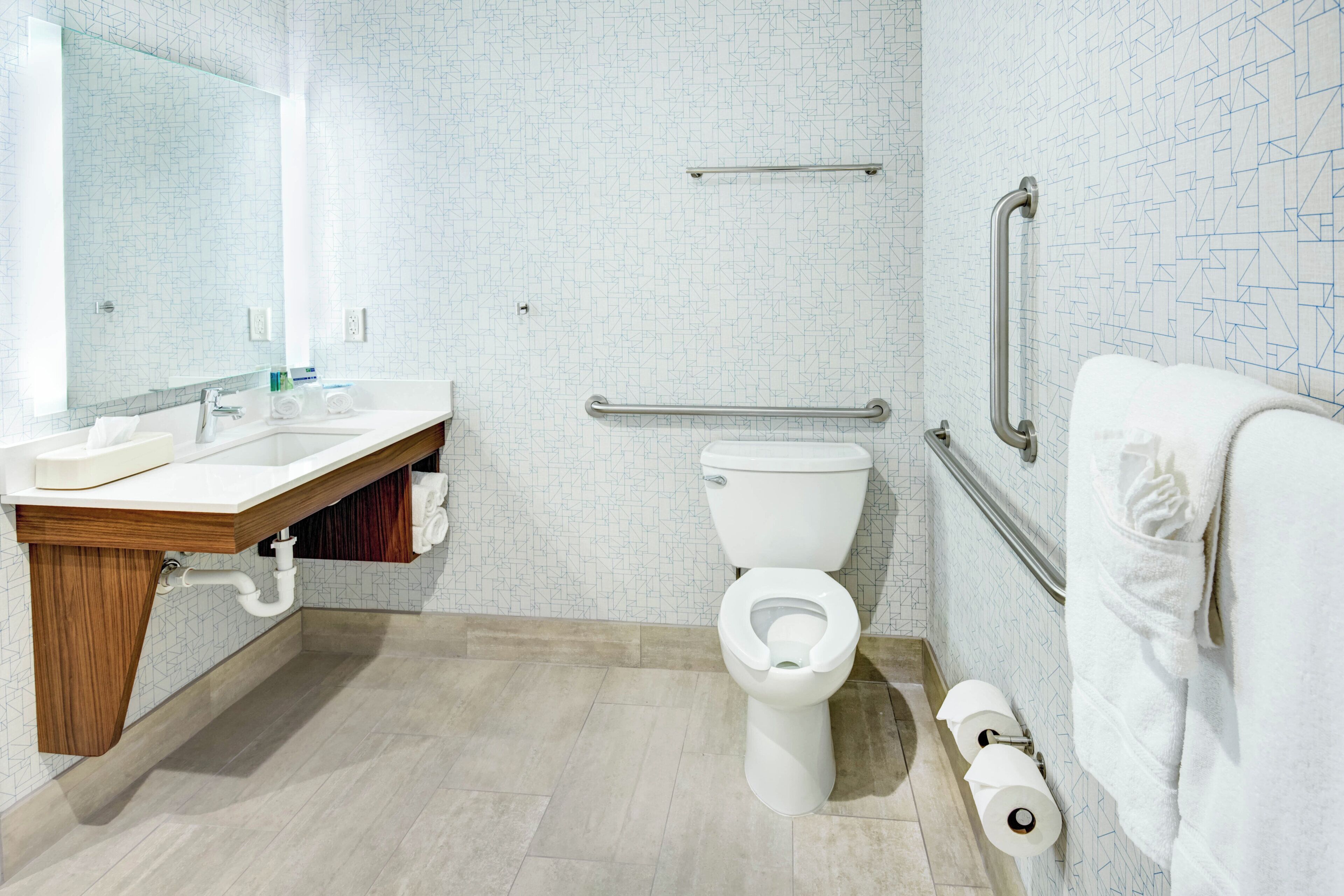 Un bany modern amb un vàter blanc, un lavabo amb taulell de fusta i un suport per a tovalloles.