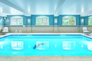 A swimming pool with clear blue water, surrounded by a tiled deck and lounge chairs. - Holiday Inn Express Woodbridge by IHG (Avenel)