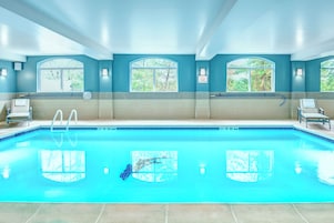 Piscina com água azul cristalina, rodeada por um deck ladrilhado e espreguiçadeiras.