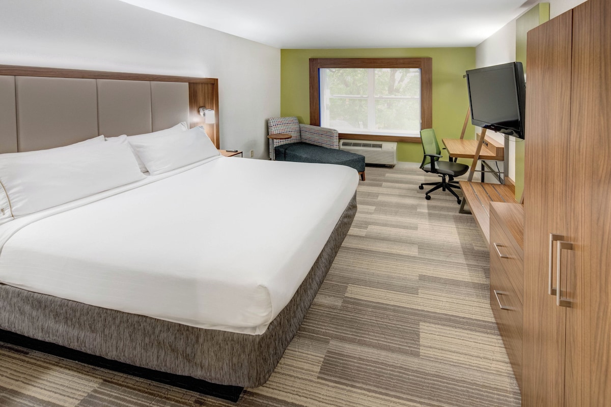 Habitación de hotel con una cama grande, un escritorio con silla, televisión y ventana.