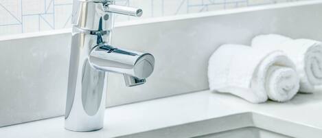 A modern bathroom with a chrome faucet, white tiles, and neatly rolled towels on a countertop.