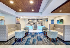 Um saguão de hotel com balcão de recepção, área de estar e um design de teto moderno.