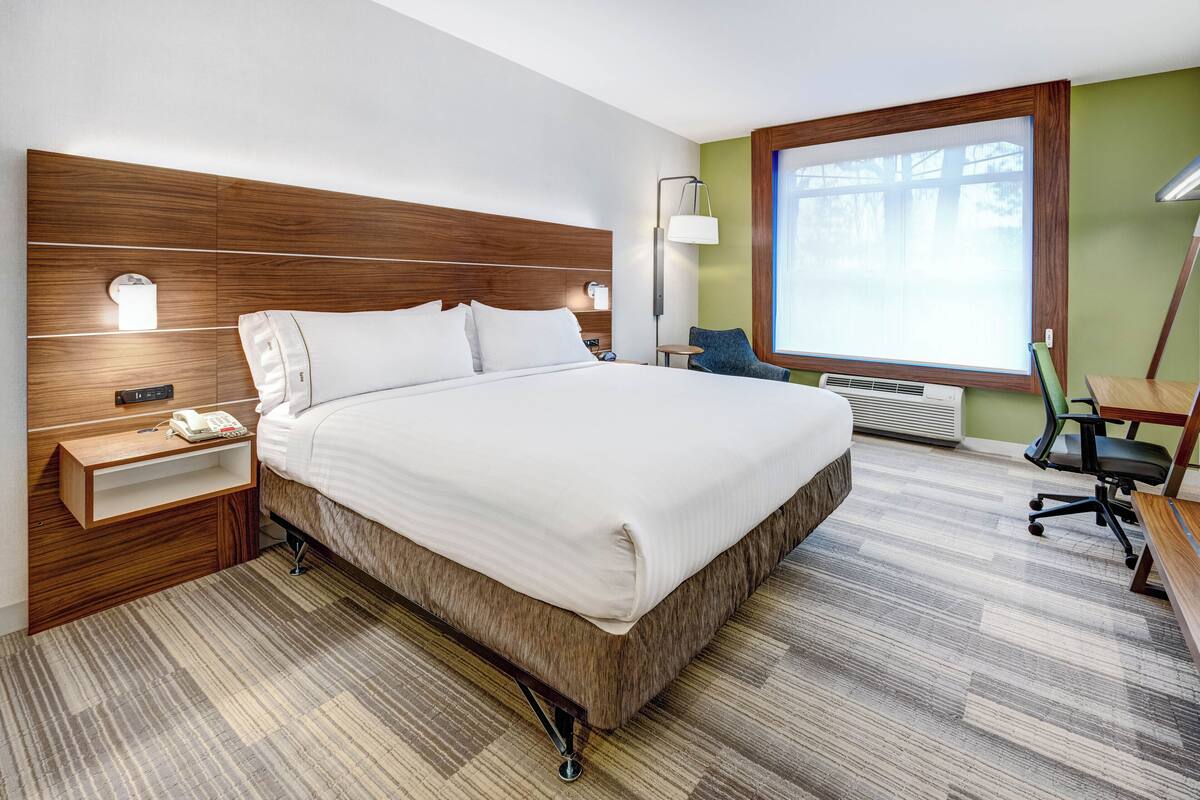 Une chambre d’hôtel moderne, dotée d’un grand lit, de tables de chevet, d’un bureau et d’une fenêtre avec des stores.